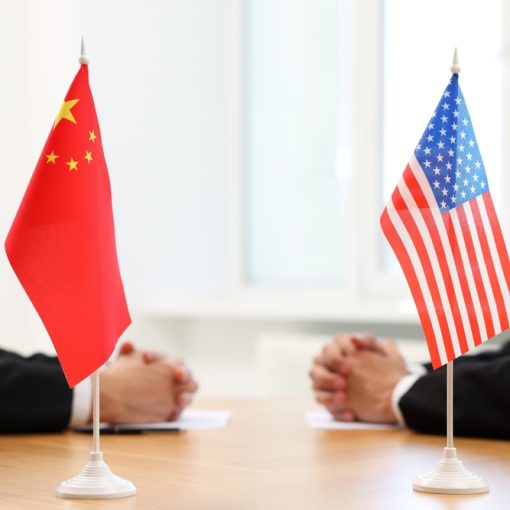 The image shows US and China flags at a negotiation table