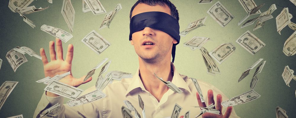 The image shows a businessman blindfolded amongst banknotes